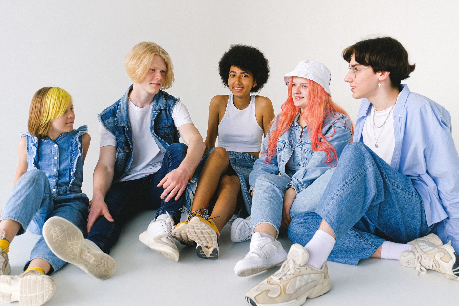 Group of cheerful diverse teenager friends talking to each other while sitting together on floor against white background — A