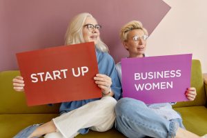 Two women on a sofa holding signs promoting startup and business women. — Cape Town Florist - Luxury Floral Designs Crafted b