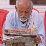 Elderly man engaging in daily reading of a newspaper while seated outdoors. — "Digital Classrooms: Top Online Learning Platfo