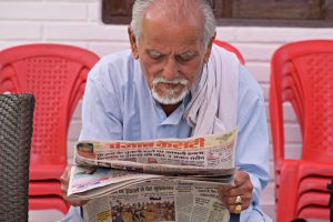 Elderly man engaging in daily reading of a newspaper while seated outdoors. — "Digital Classrooms: Top Online Learning Platfo