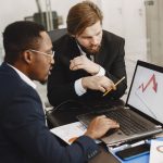 Two business professionals discuss marketing data on a laptop in a modern office. — Elements Brasserie: Enjoy a Perfectly Gri