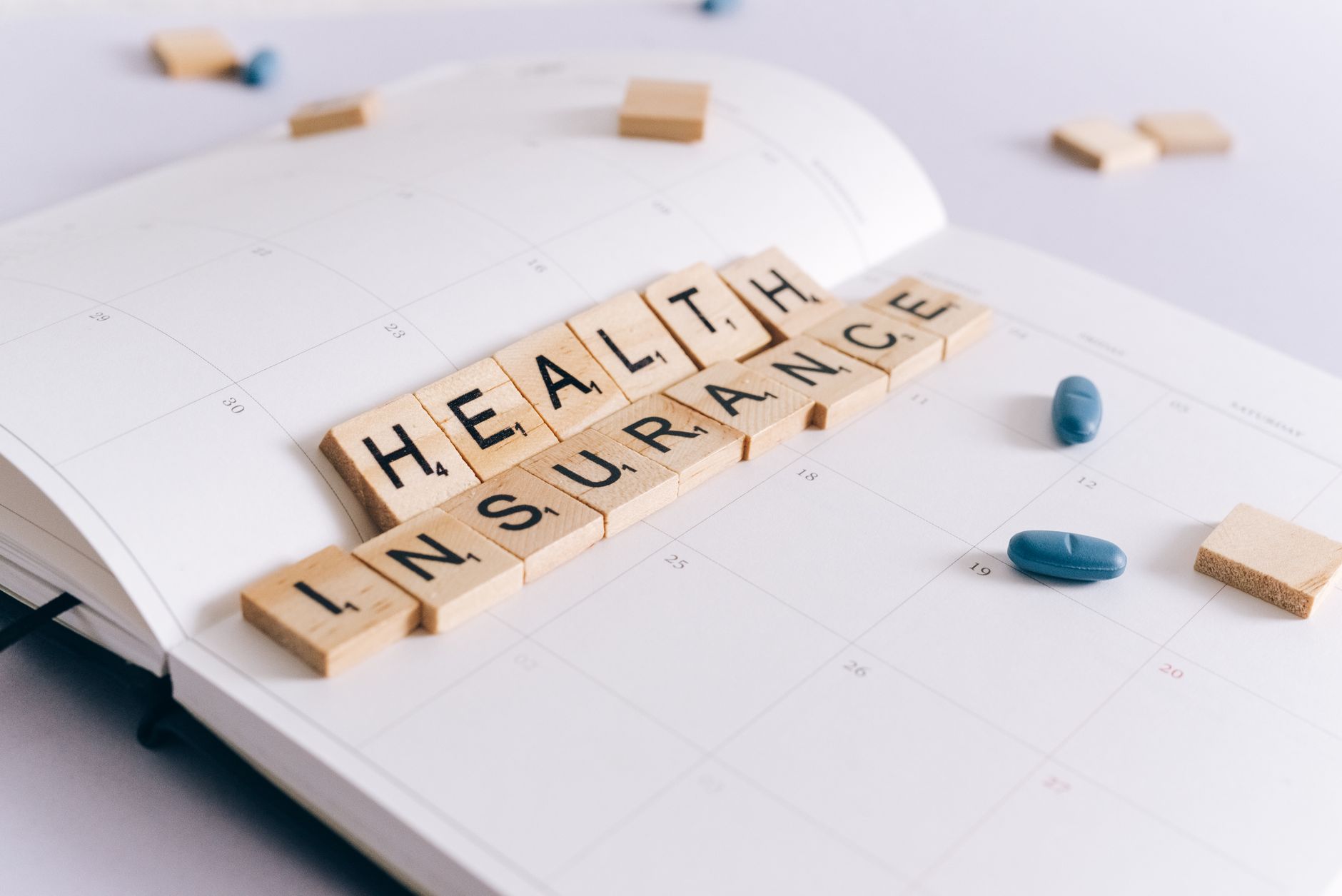 Scrabble tiles spelling 'Health Insurance' on a calendar with pills. — Expert Heart Health Advice from Dr Ian Weisberg on Pal