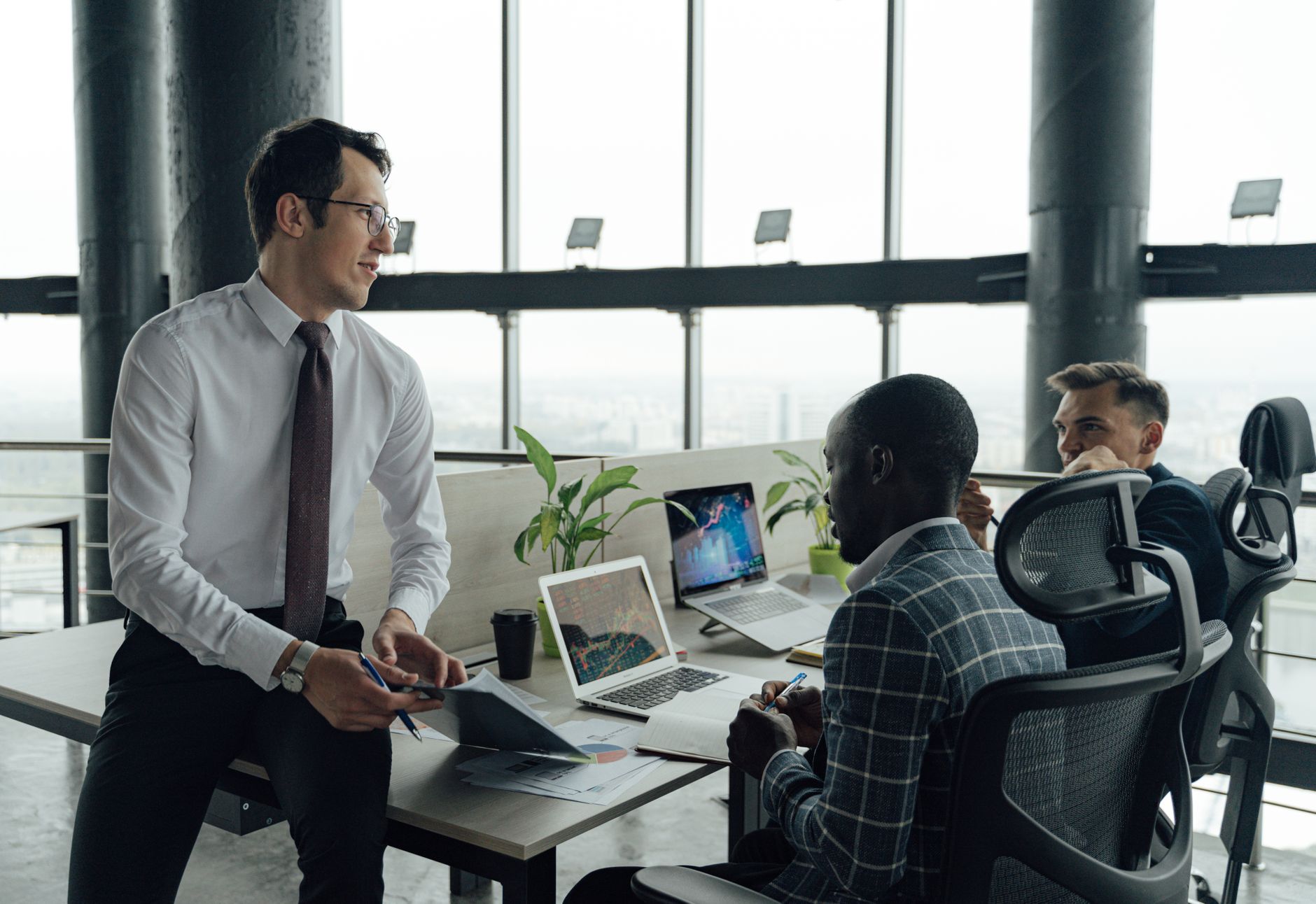Three men engaged in a business meeting in a modern office setting with laptops and documents. — Find Affordable Cannabis Pro