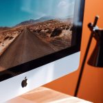 A sleek modern workspace featuring an iMac displaying a desert road and a stylish desk lamp. — How a Simple YouTube Video Emb