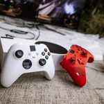 White and red wireless gaming controllers on a textured surface near chips and a TV screen. — KOITOTO: Your Premier Choice fo