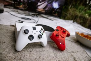 White and red wireless gaming controllers on a textured surface near chips and a TV screen. — KOITOTO: Your Premier Choice fo