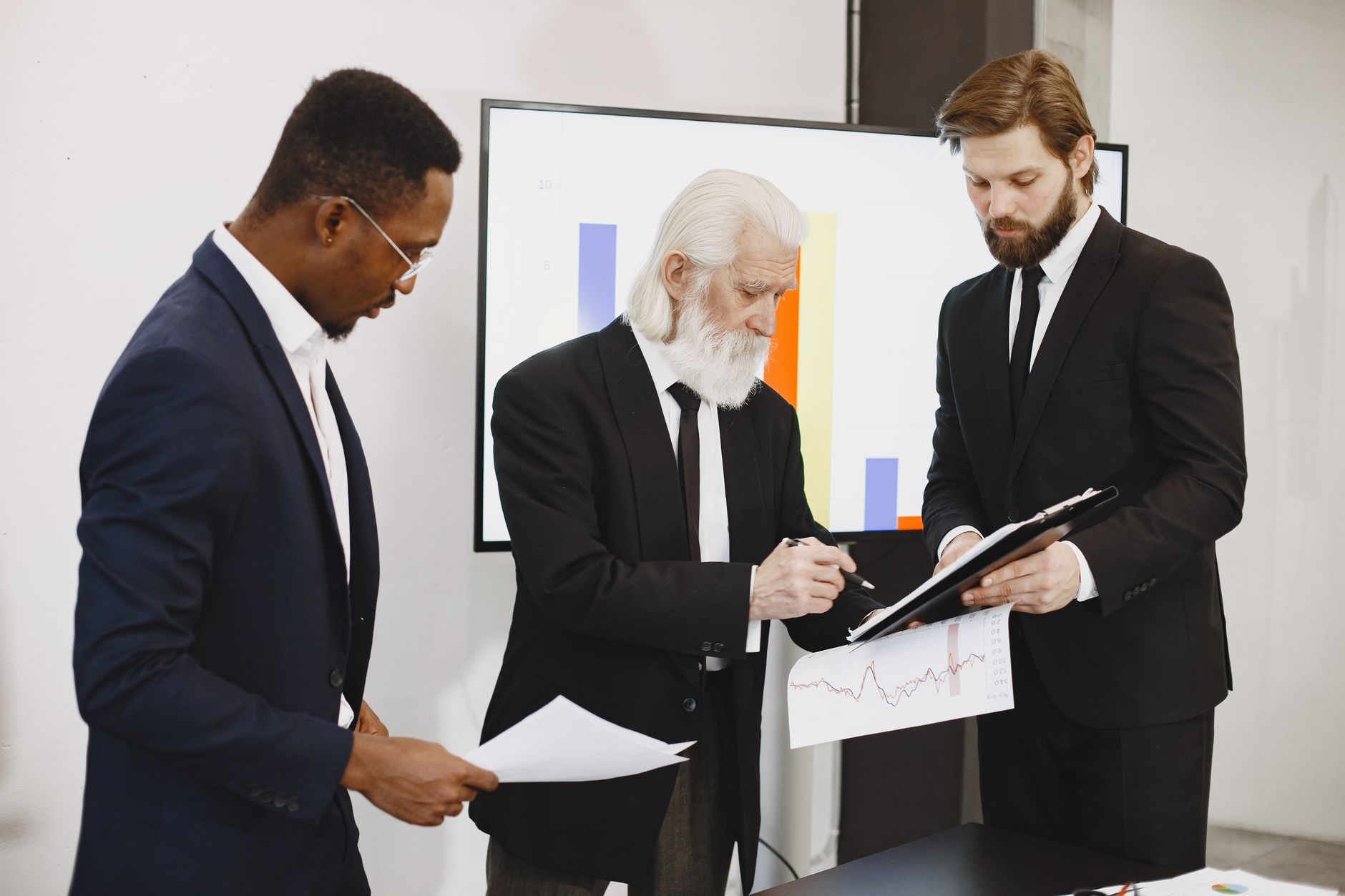 Three businessmen in suits reviewing reports and graphs during an office meeting. — Madrid Zoo Aquarium Adventures for Every