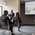 A business professional delivering a presentation in a conference room with diverse attendees. — Success Stories: From Part-T