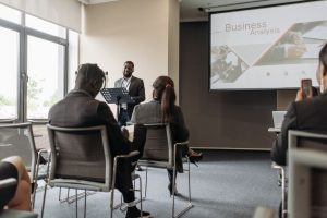 A business professional delivering a presentation in a conference room with diverse attendees. — Success Stories: From Part-T