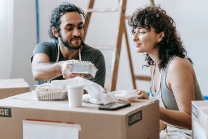 A couple relaxes with takeout food amidst moving boxes in their new home. — Understanding the Psychology Behind Football Bett