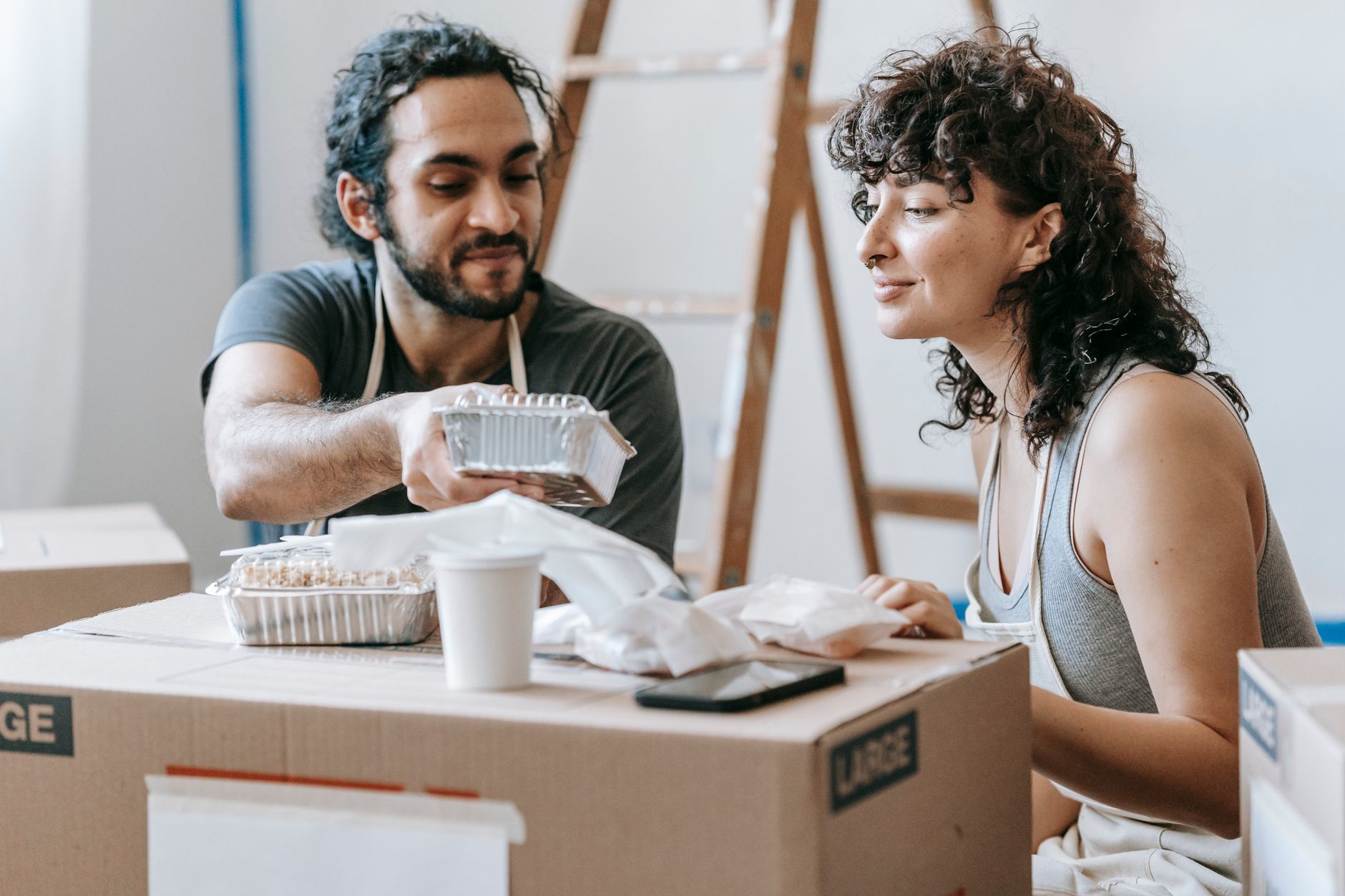 A couple relaxes with takeout food amidst moving boxes in their new home. — Understanding the Psychology Behind Football Bett